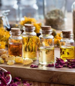 Bottles of essential oil with dried rose petals, chamomile, calendula and frankincense resin on a wooden table